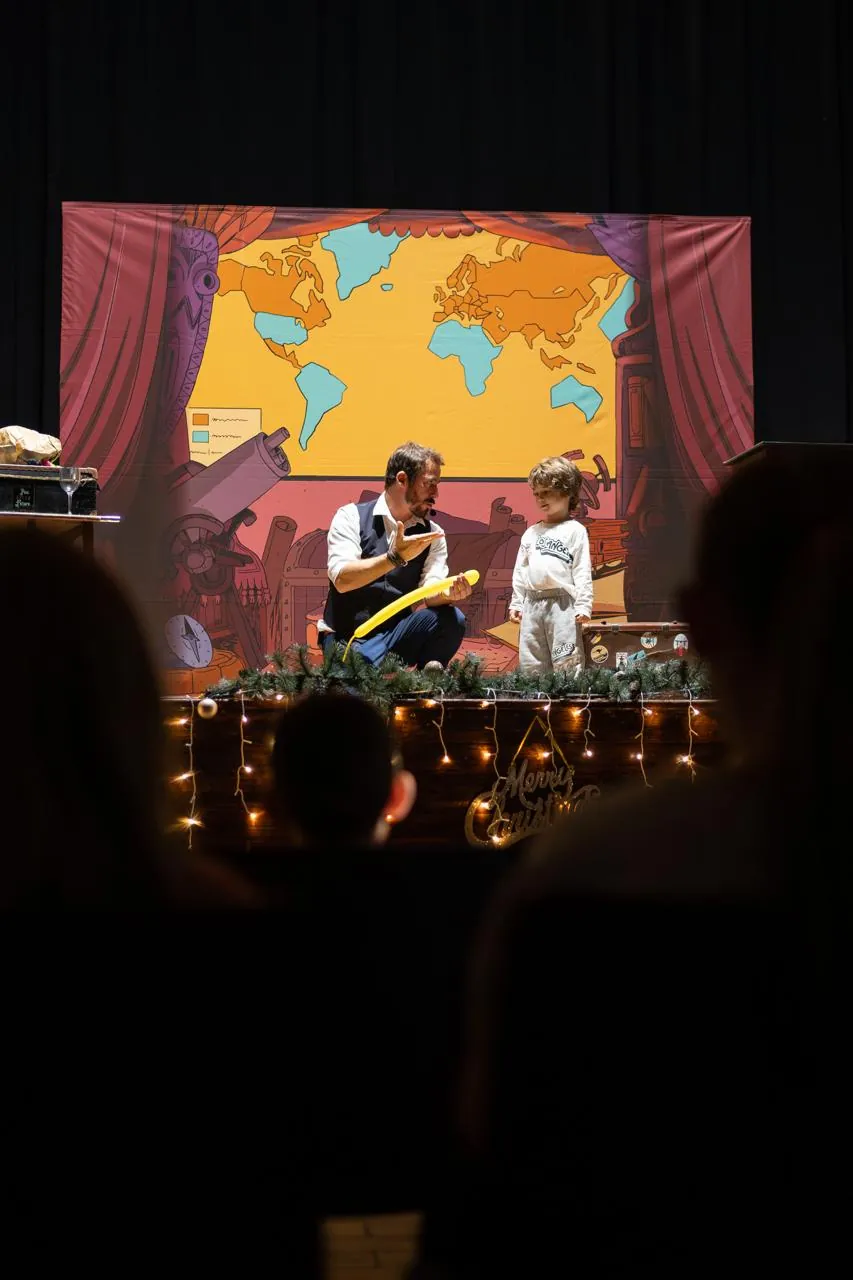 Wicka, magicien, sur scène avec un enfant volontaire pendant le spectacle de l'arbre de Noël d'une entreprise