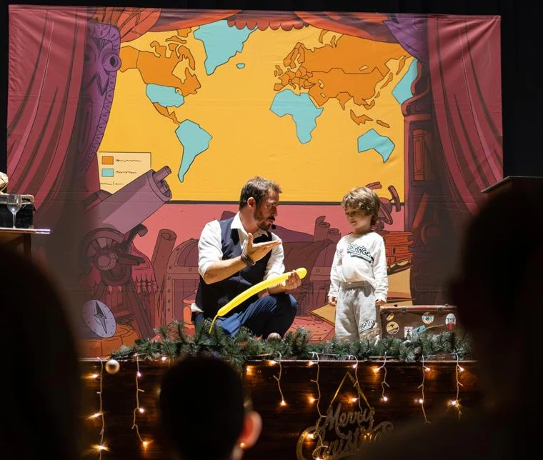 Wicka fait monter un enfant sur scène pendant un spectacle de Noël Chercheur d'Impossible
